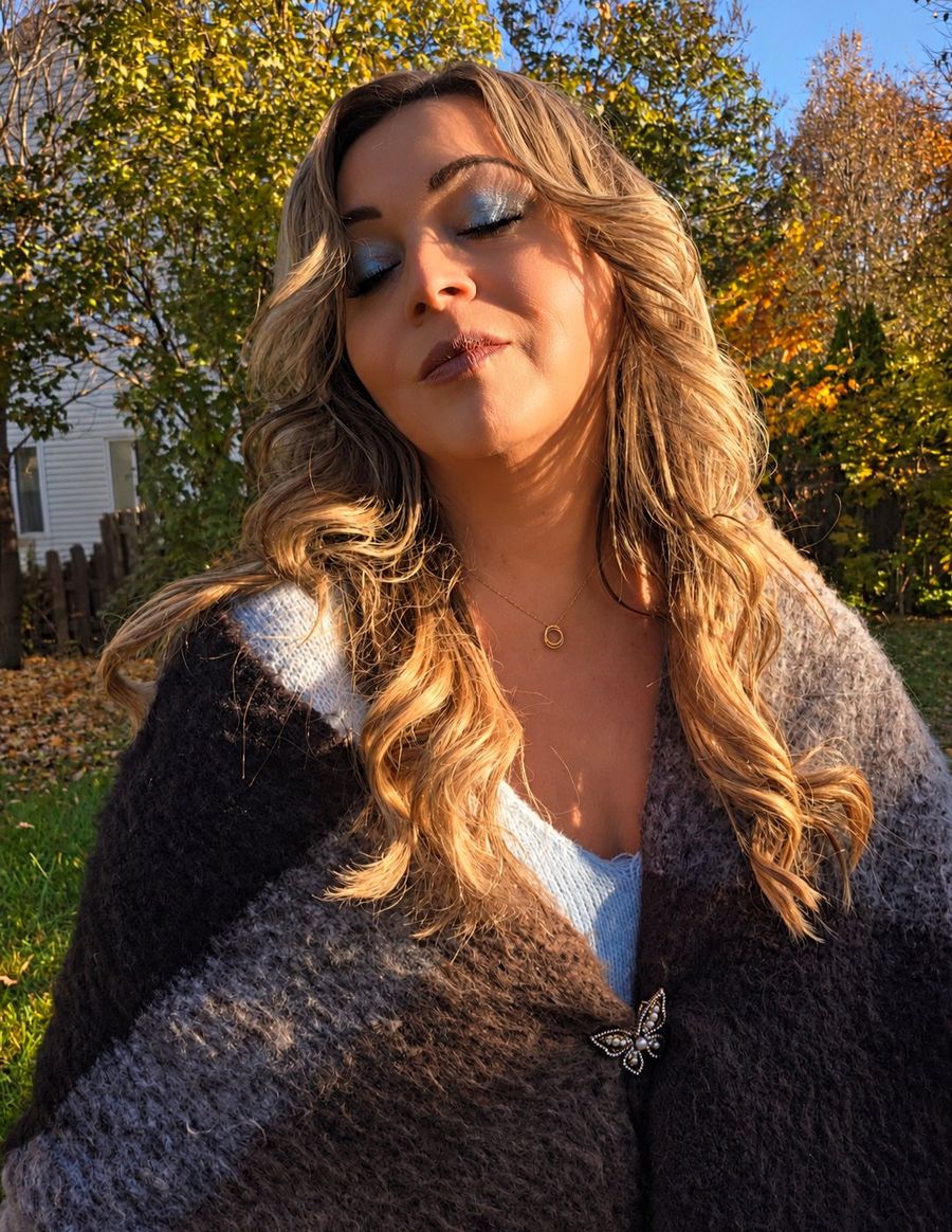 Portrait d’automne de Cindy Roy, les yeux fermés dans la lumière dorée du soleil, cardigan brun et gris fermé par sa broche papillon