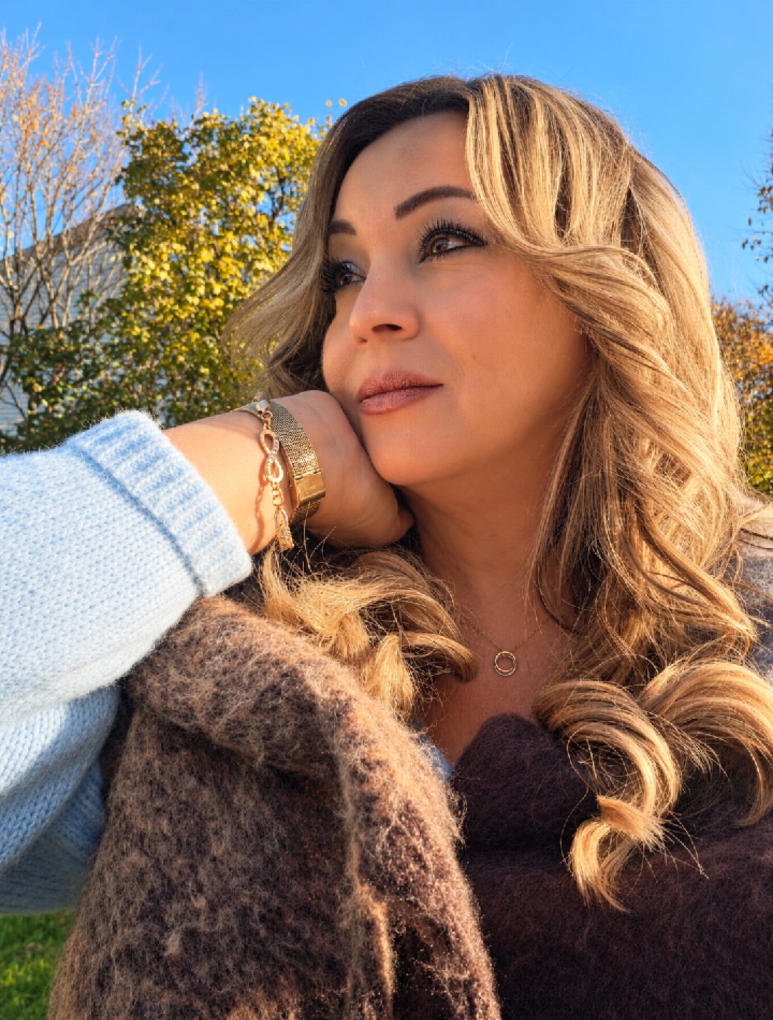 Cindy Roy de profil, le menton appuyé sur sa main — montre et bracelet dorés — sous un ciel bleu d’automne