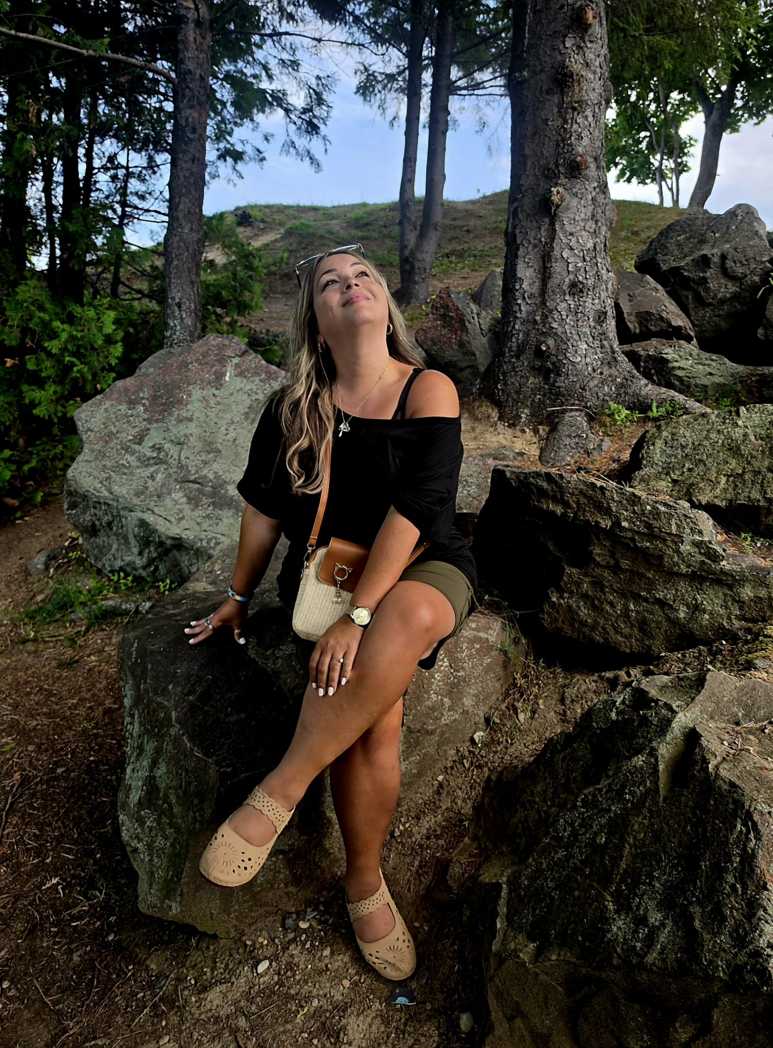 Cindy Roy assise sur un rocher entre les pins, le regard levé vers le ciel