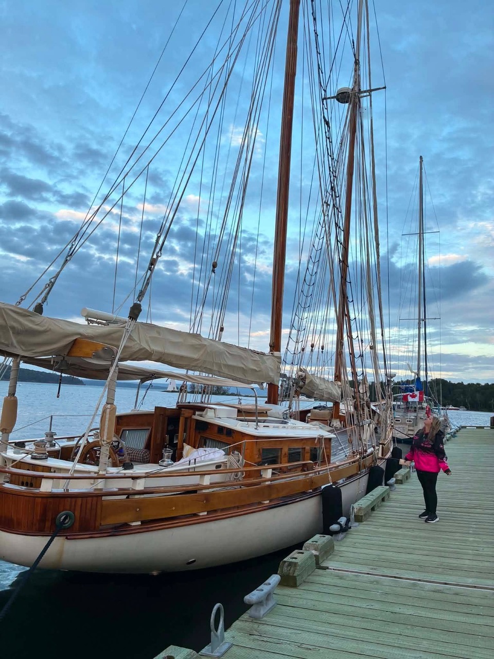 Un grand voilier de bois amarré au quai au crépuscule, avec Cindy Roy à côté, en rose, la main posée près du bateau
