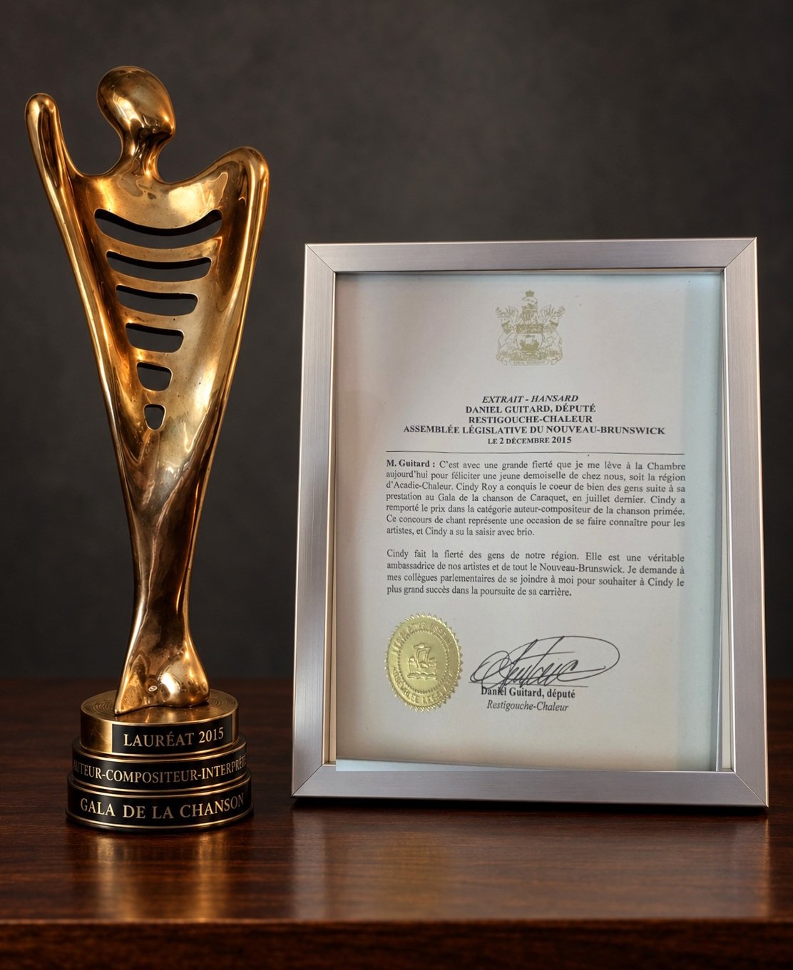 Le trophée Lauréat 2015 du Gala de la chanson de Cindy Roy, à côté de l’extrait encadré du hansard de l’Assemblée législative du Nouveau-Brunswick du 2 décembre 2015 où le député Daniel Guitard lui rend hommage